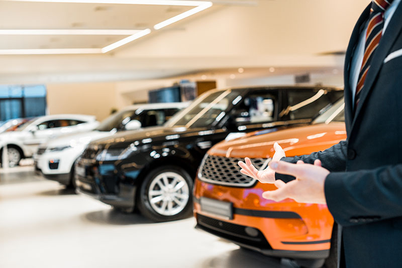 Cropped Image Of Male Car Dealer Pointing By Hands In Car Salon